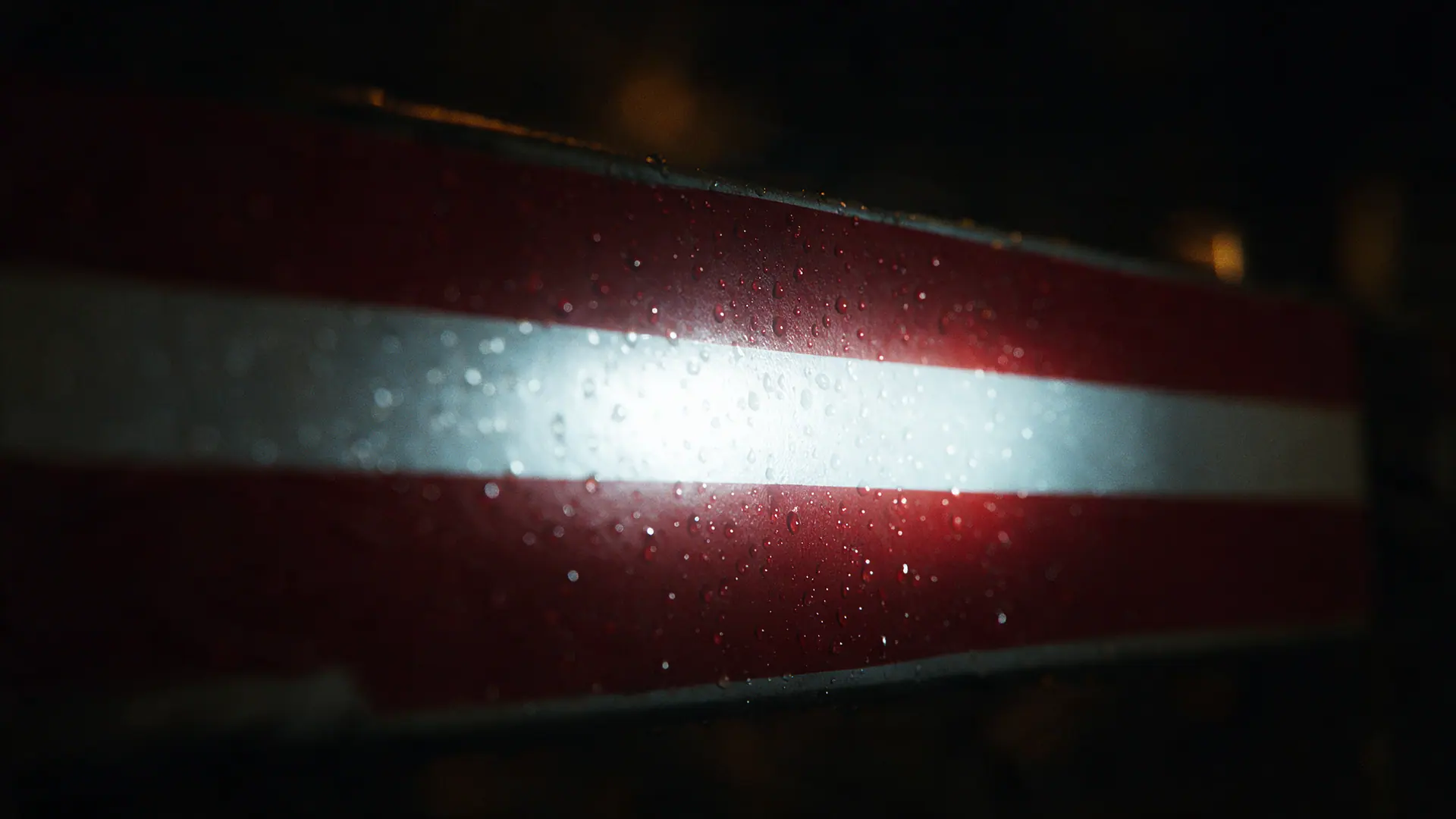 Nahaufnahme des retroreflektierenden weißen Streifens einer rot-weißen Leitbake, von einem Scheinwerfer angestrahlt, mit Regentropfen auf der Folie. Bildmotiv KI-generiert.