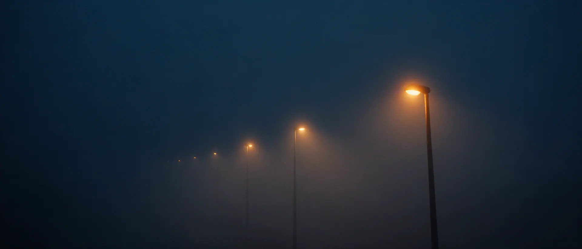 Reihe von Autobahnleuchten im Nebel, die Lichtpunkte verlieren sich nach hinten im Dunst. Bildmotiv KI-generiert.
